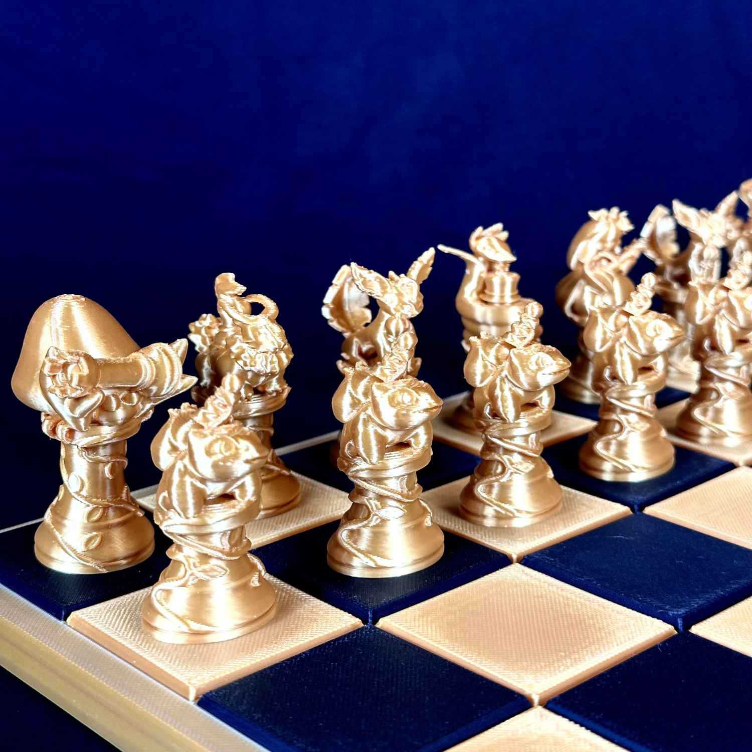 Pièces d’échecs dorées originales Chess Project alignées sur un échiquier bleu et or, vue de côté mettant en valeur le design détaillé et la finition élégante.