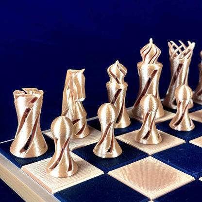 Pièces d’échecs twist dorées Chess Project alignées sur un échiquier bleu et or, vue de côté mettant en valeur les formes torsadées et le design sculptural.